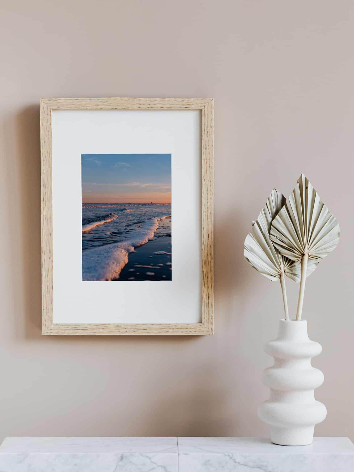 photo by Celebrate Again of ocean waves at sunset hanging on a wall in a wooden frame next to a paper plant decor for a yoga space at home
