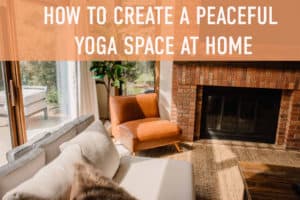 "how to create a peaceful yoga space at home" text over a view of a living room with a cozy couch chair and fire place as the light streams in from the big windows