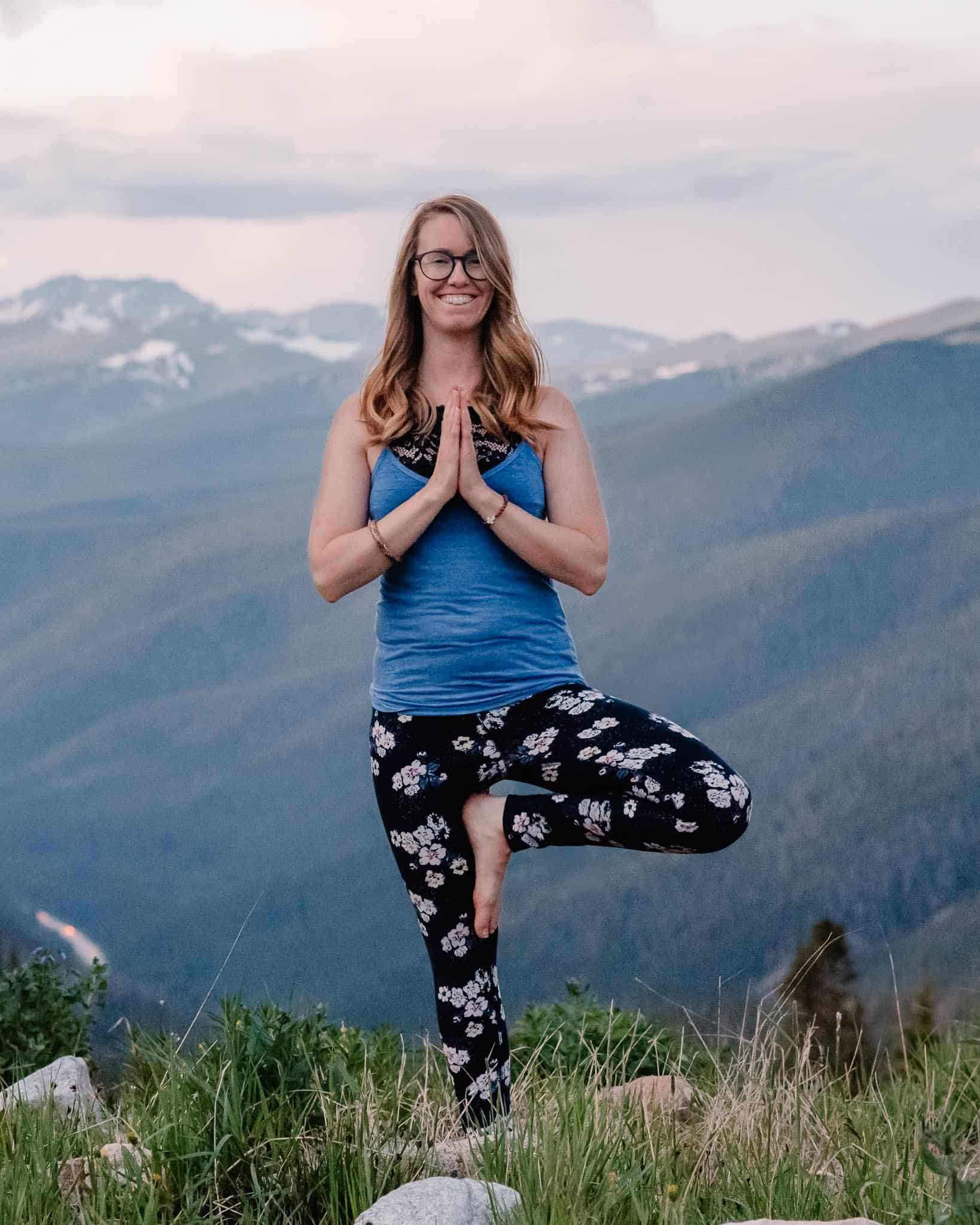 emmy doing yoga for tight shoulders on the top of a mountain doing tree pose with hands in namaste
