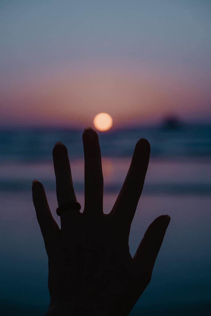 hand up with the illusion of a finger touching the setting sun on a colorful ocean sunset