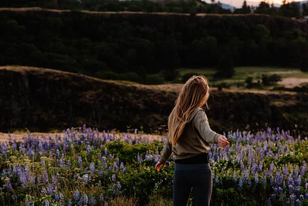 person with arms out wide in a wild flower field