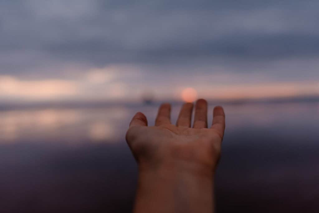 hand reaching out to touch sunset