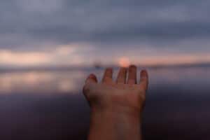 hand reaching out to touch sunset